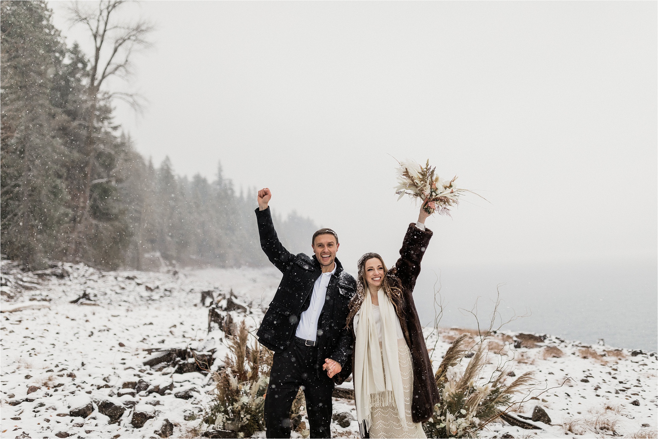 Wedding couple holding up hands cheering after their ceremony in the snow