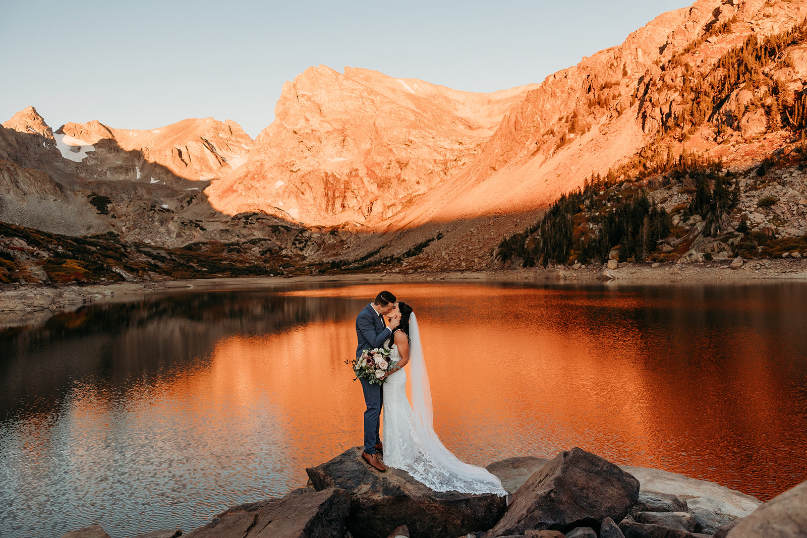 bride and groom hug on a rock overlooking a lake
