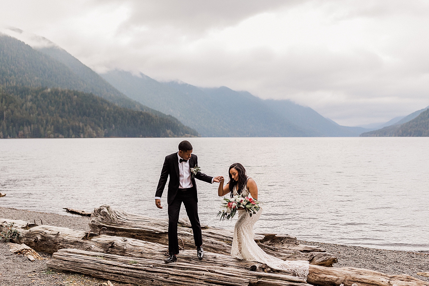 Groom helping his bride over the driftwood at Lake Crescent. Photo by Megan Montalvo Photography.