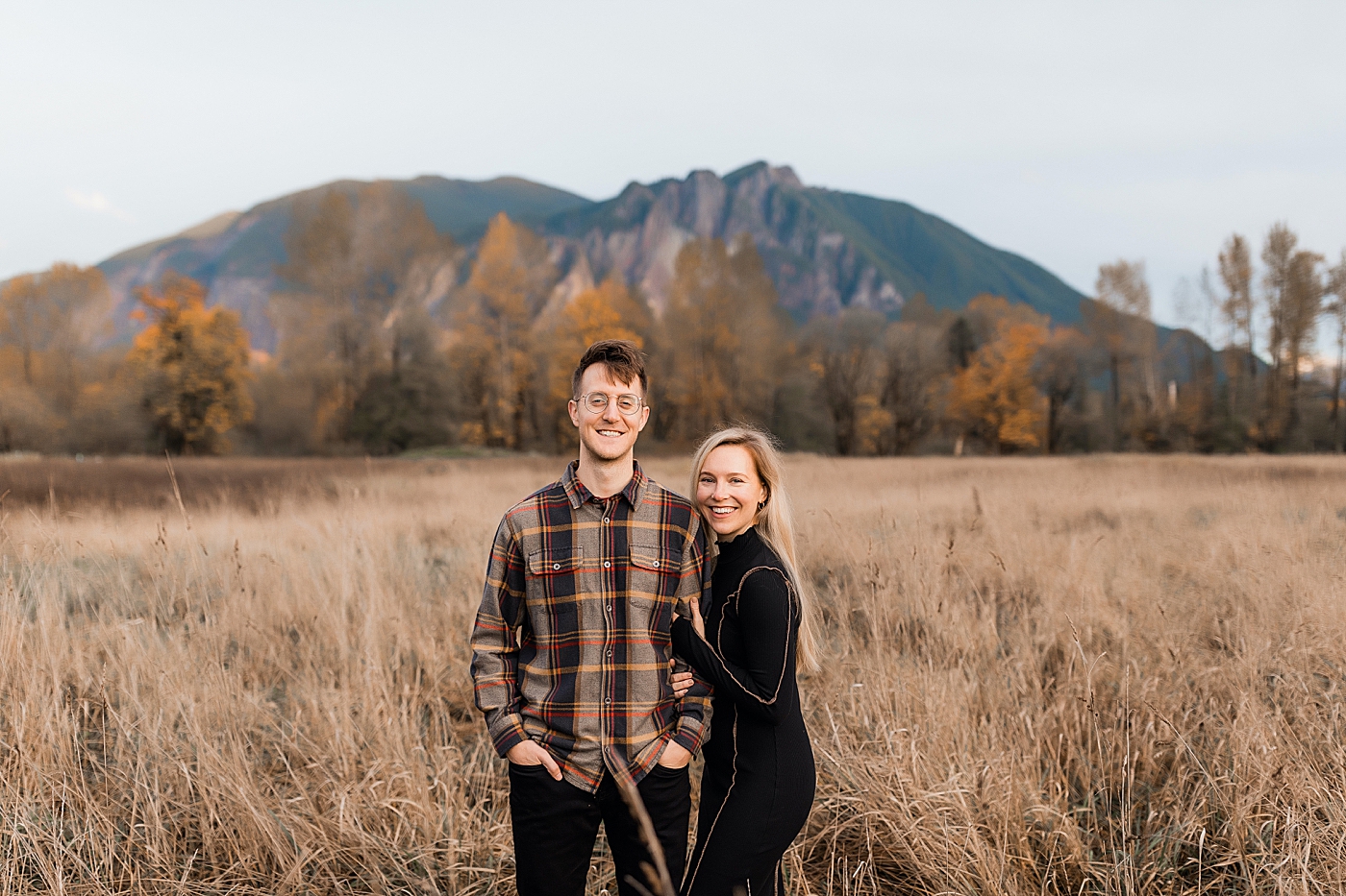 Couple standing in a field in front of Mount Si. Photo by Megan Montalvo Photography.