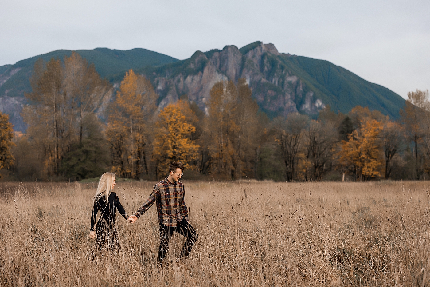 Couple walking through field in front of Mount Si. Photo by Megan Montalvo Photography.