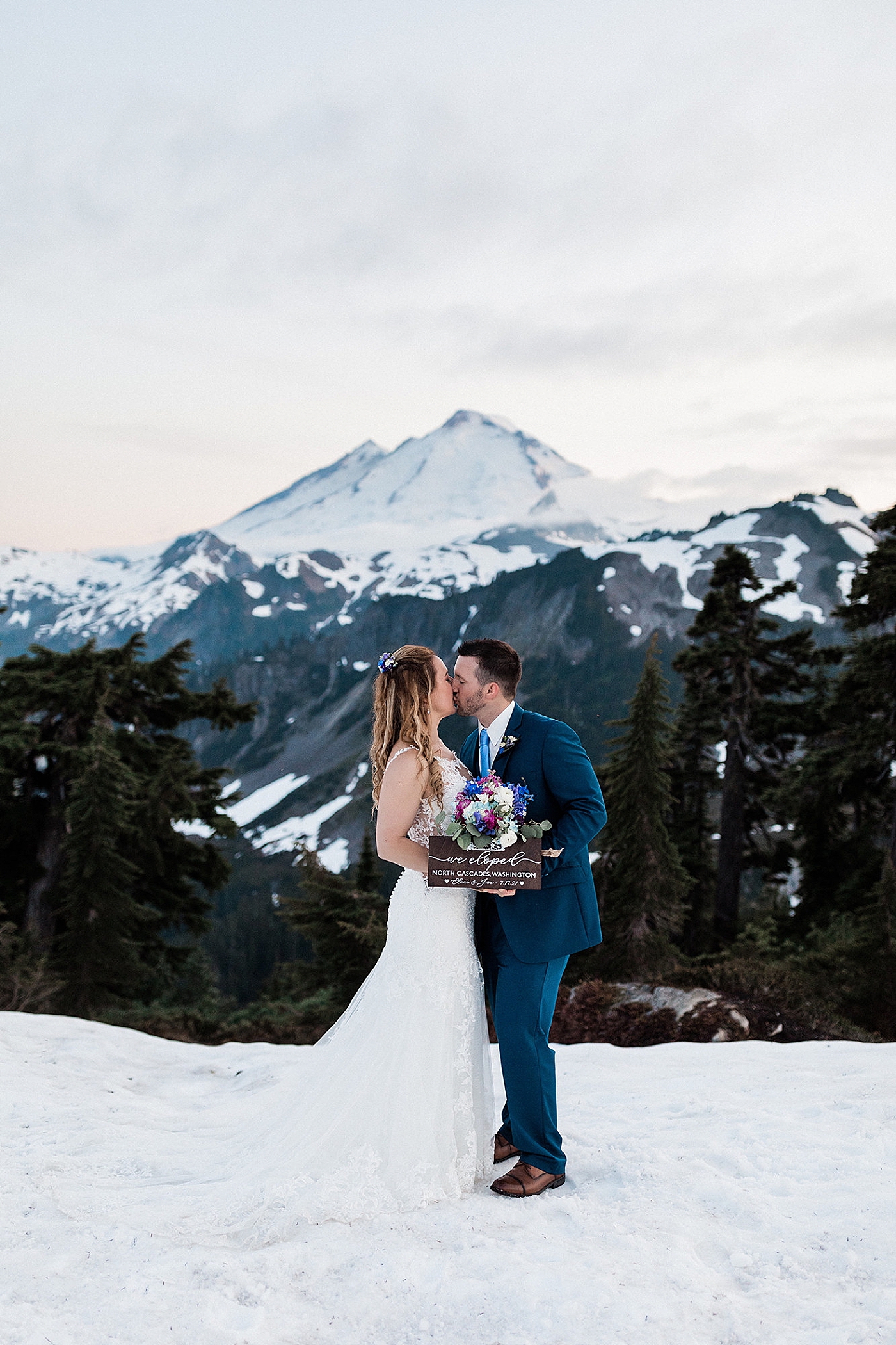 Couple kissing in the snow with elopement sign. Photo by Megan Montalvo Photography.