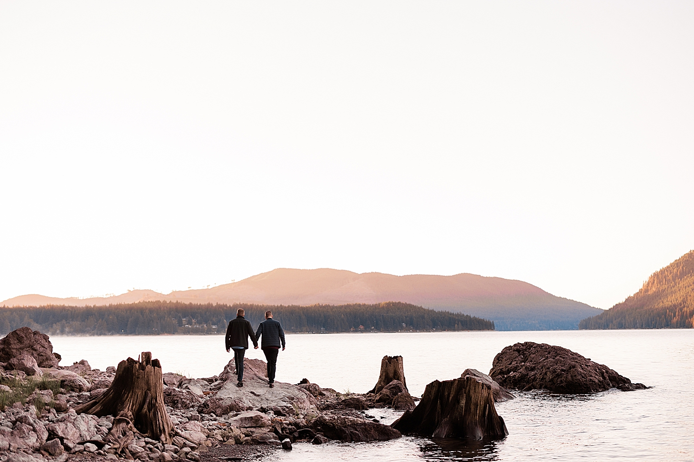 Couple holding hands walking out the rocks into a beautiful sunrise. Photo by Megan Montalvo Photography.