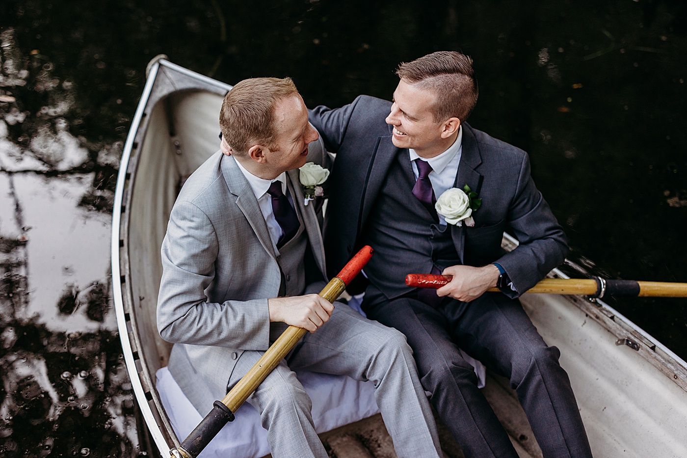 Grooms looking at each other while sitting in small boat at Sanders Estate | Megan Montalvo Photography
