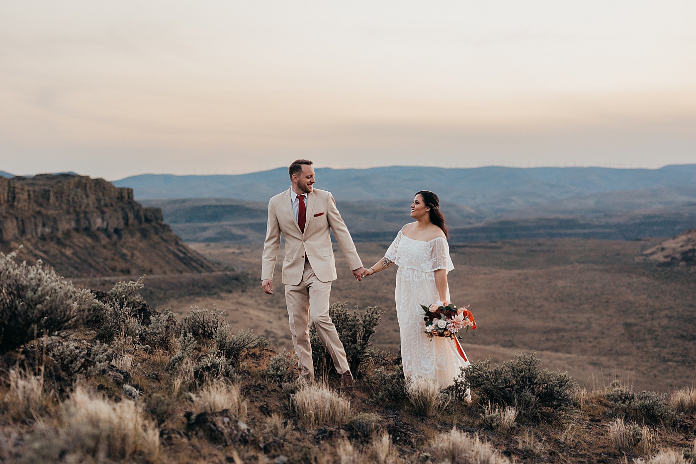 Bride and groom holding hands walking through the desert at Vantage | Photo by Megan Montalvo Photography
