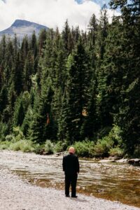 groom stands at edge of river looking into nature