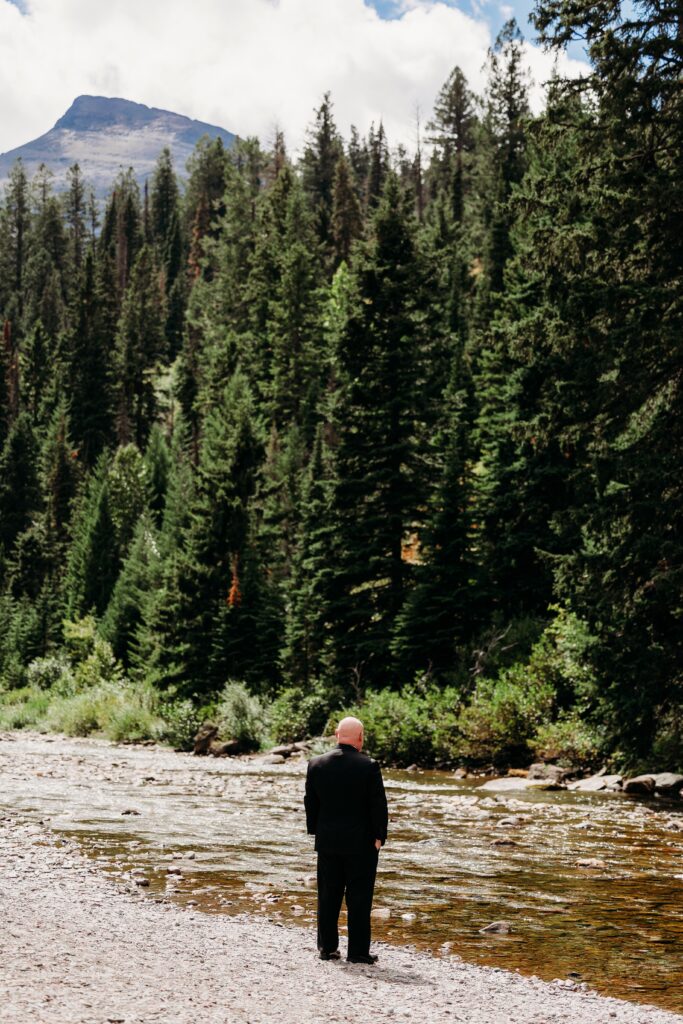 groom stands at edge of river looking into nature