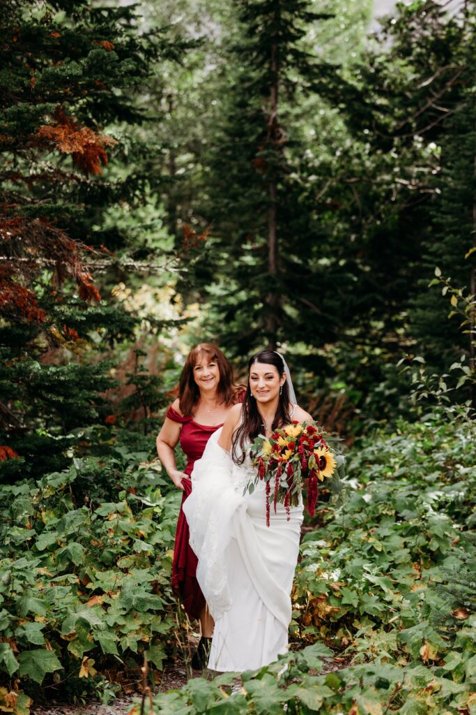 bride walks through greenery with woman carrying her train
