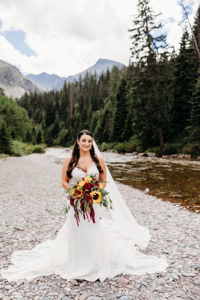 bride stands in front of river holding fall-inspired bouquet