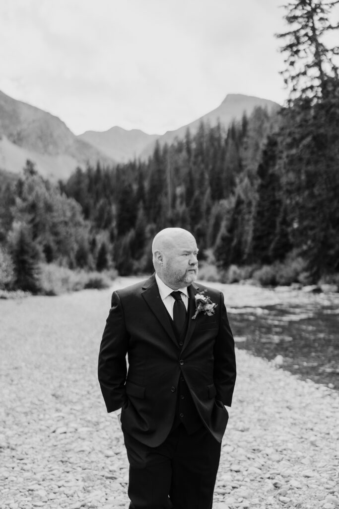 groom stands looking out towards nature with his hands in his pockets