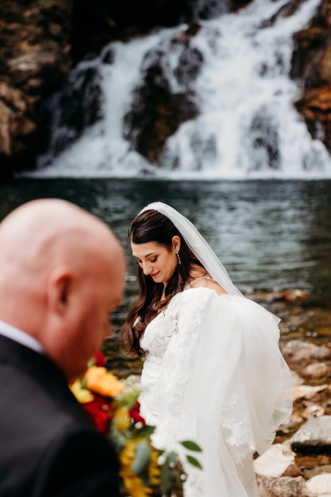 bride and groom stand looking down in front of a waterfall