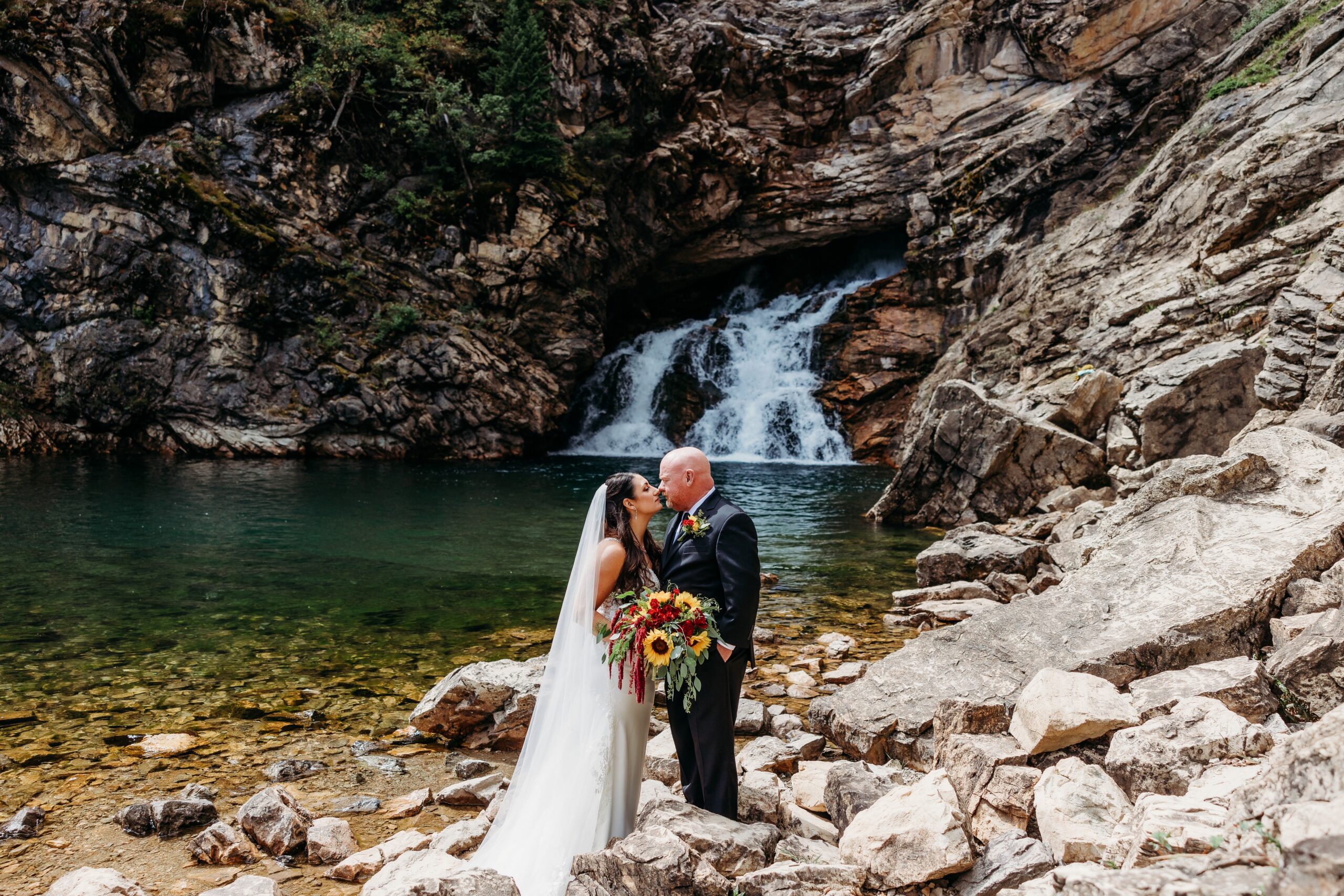 bride and groom kiss in front of waterfall