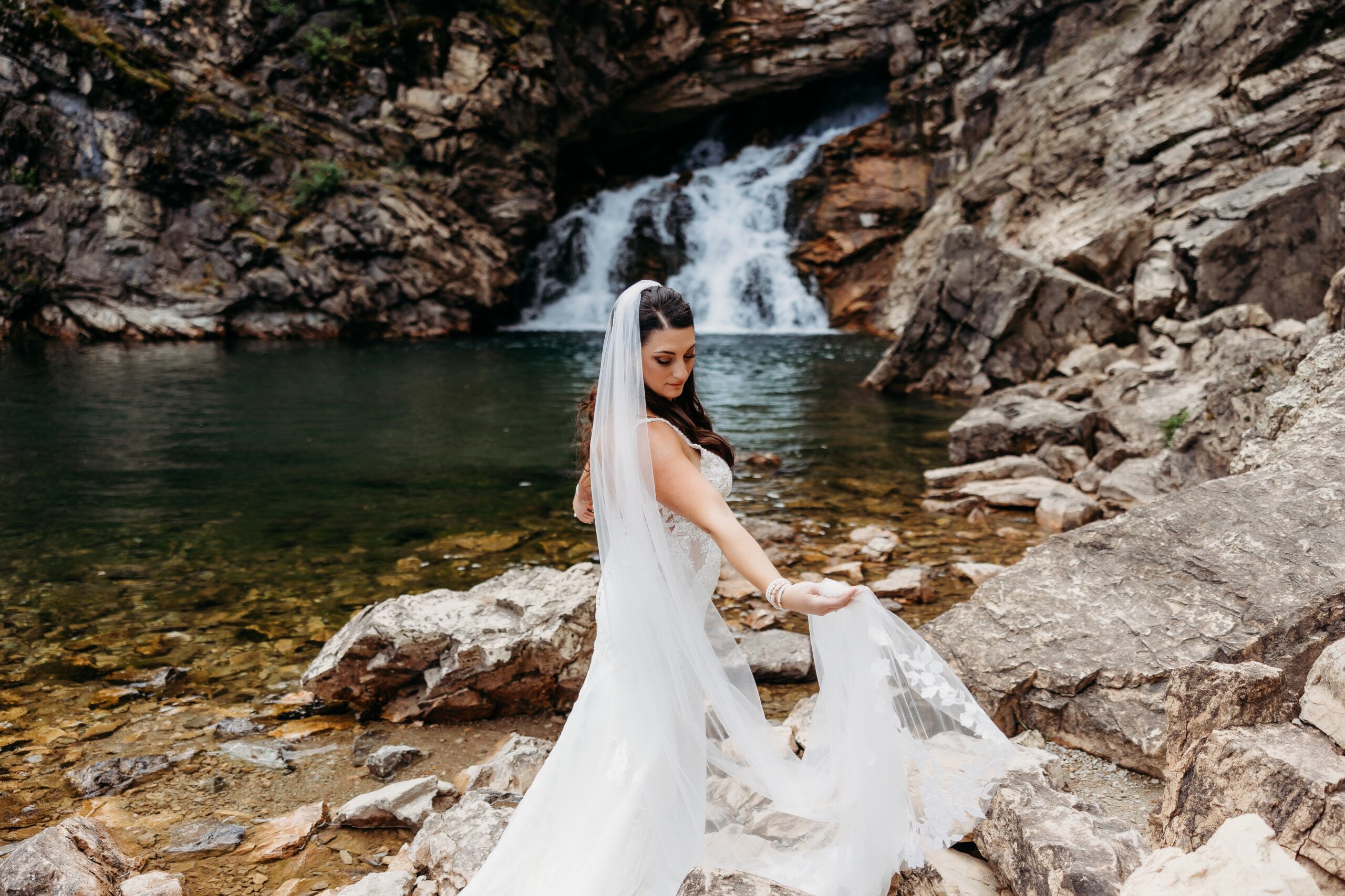 bride plays with dress in front of waterfall at glacier national park
