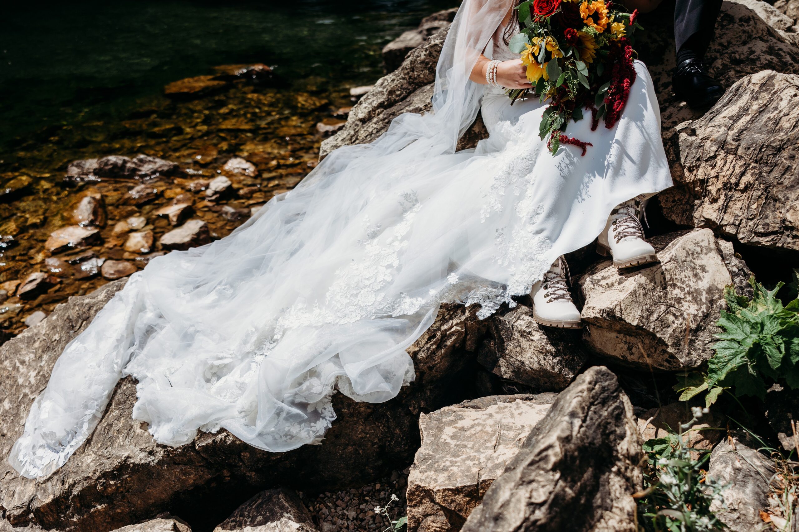 bride sits on rocks near water's edge