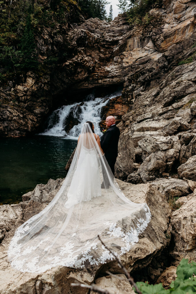 bride and groom stand on rocks over looking waterfall