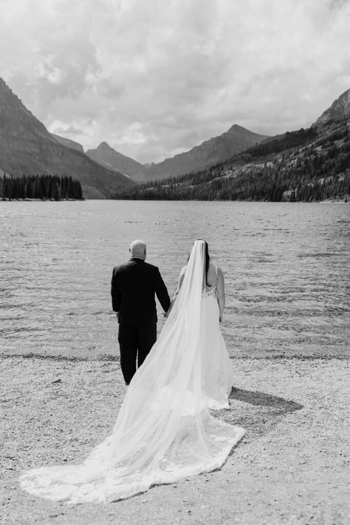bride and groom hold hands and stand at edge of lake