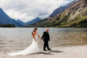 bride and groom hold hands and walk along water's edge at pray lake