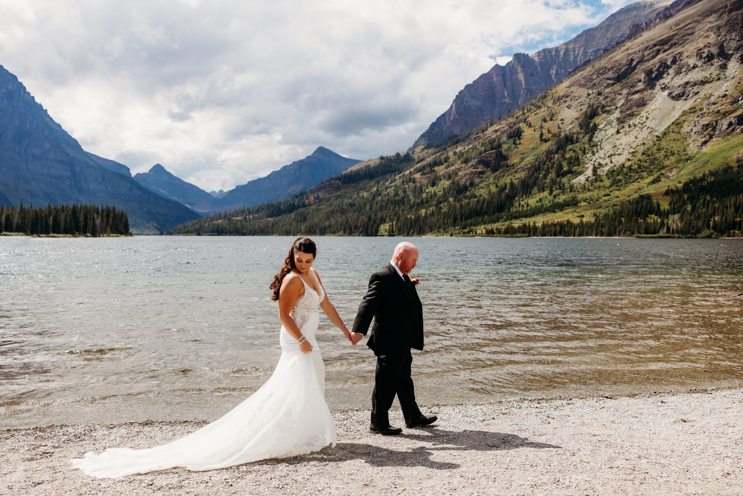 bride and groom hold hands and walk along water's edge at prayer lake