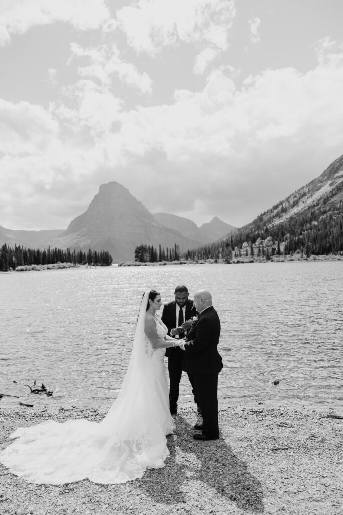 bride and groom stand lakeside during ceremony at glacier national park