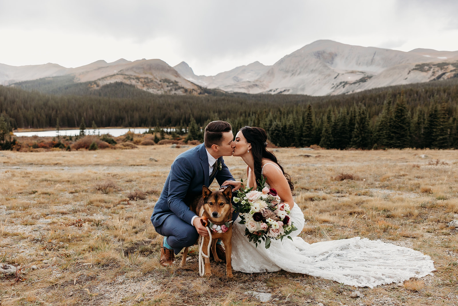 bride and groom with their dog in front of the mountains