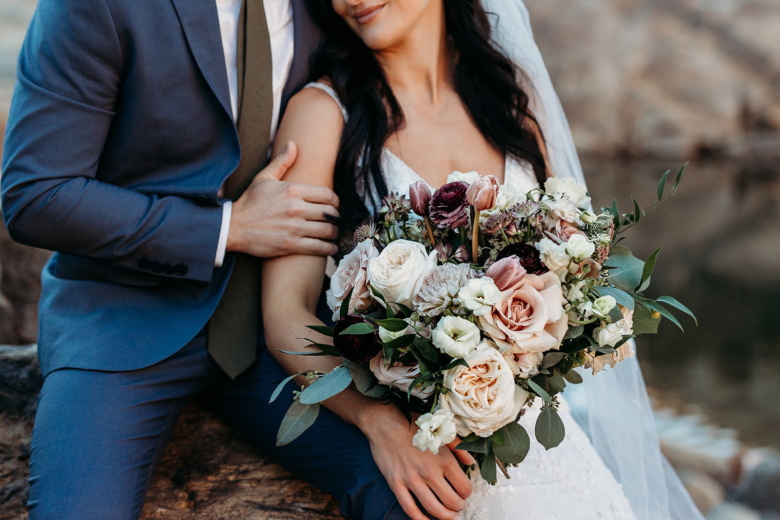 groom holds brides arm as she holds white, blush and dark purple bridal bouqet