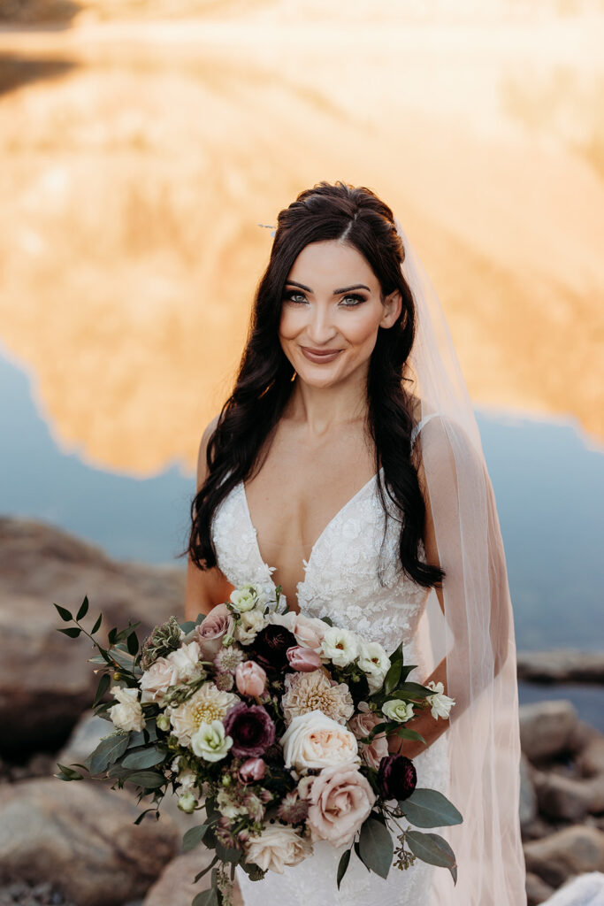 bride smiles while holding white, blush, burgundy bridal bouquet 