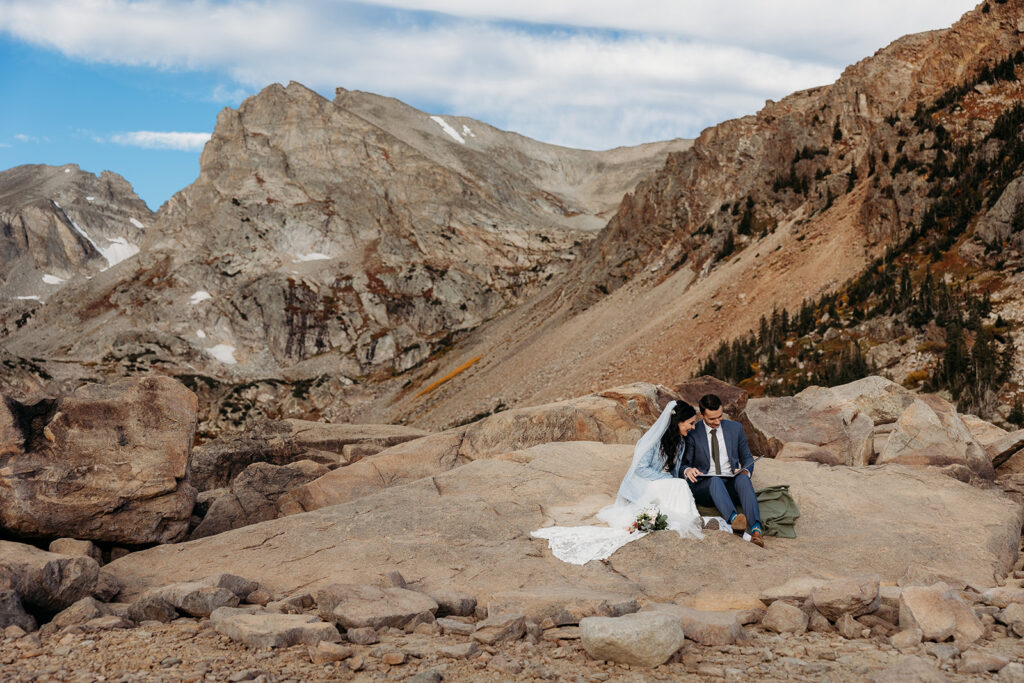 bride and groom sit on rock together in the sun