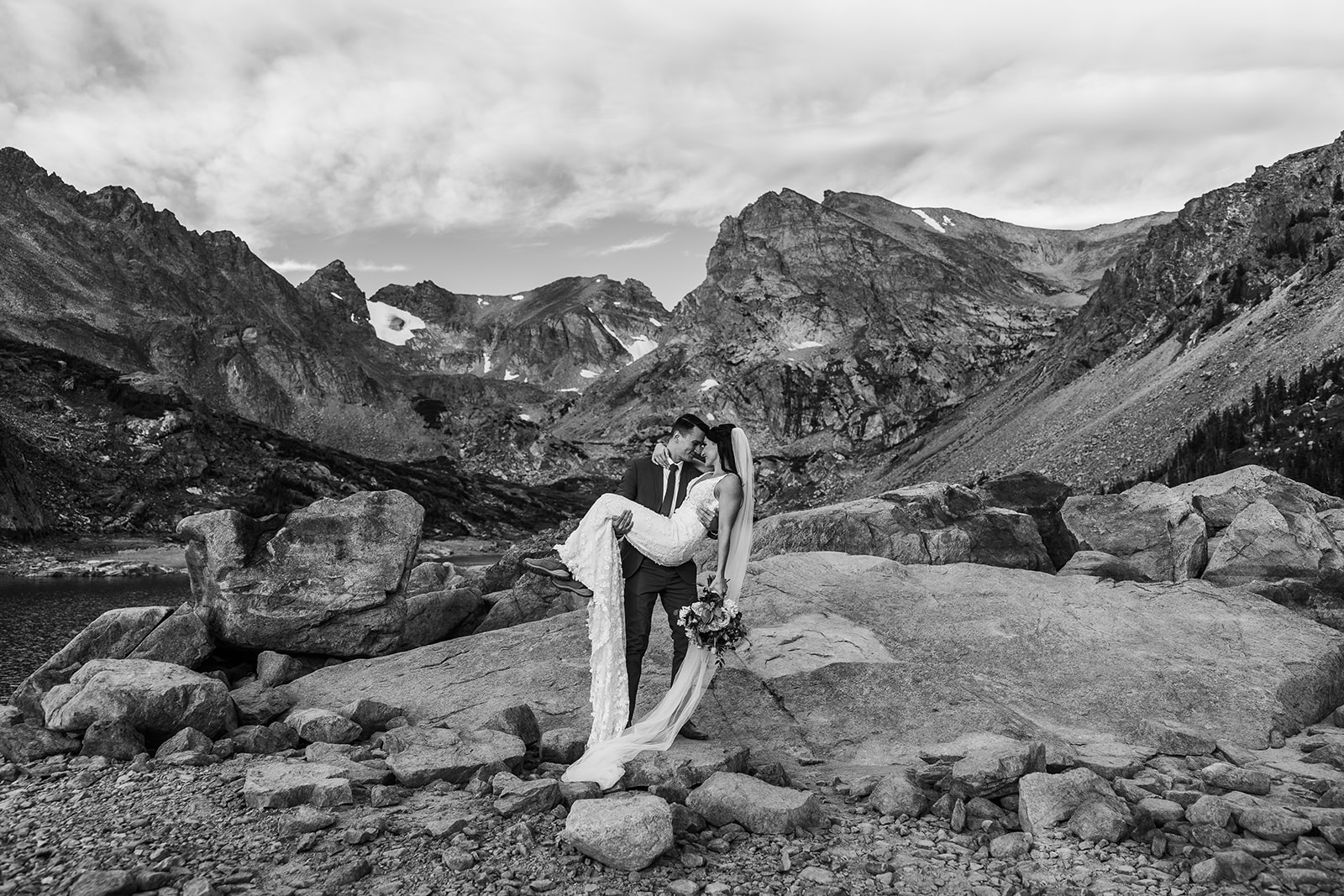 groom holds bride in front of mountain range