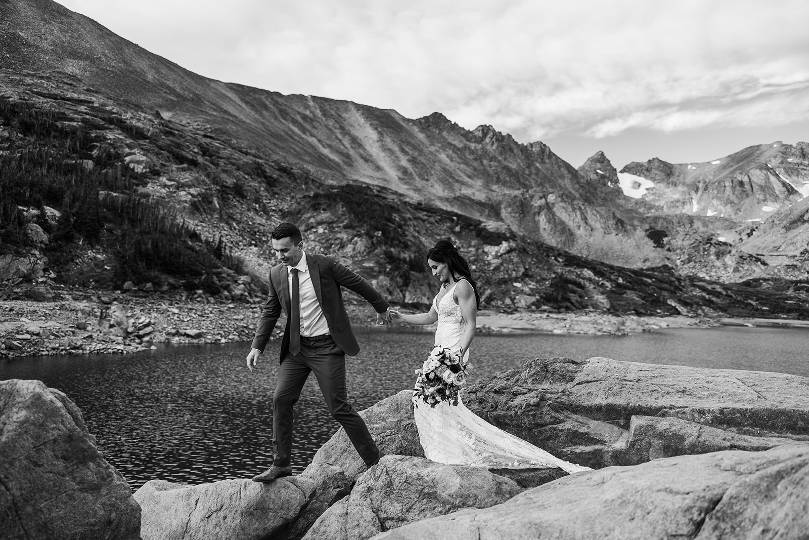 bride and groom walk along rocks in front of lake in Colorado