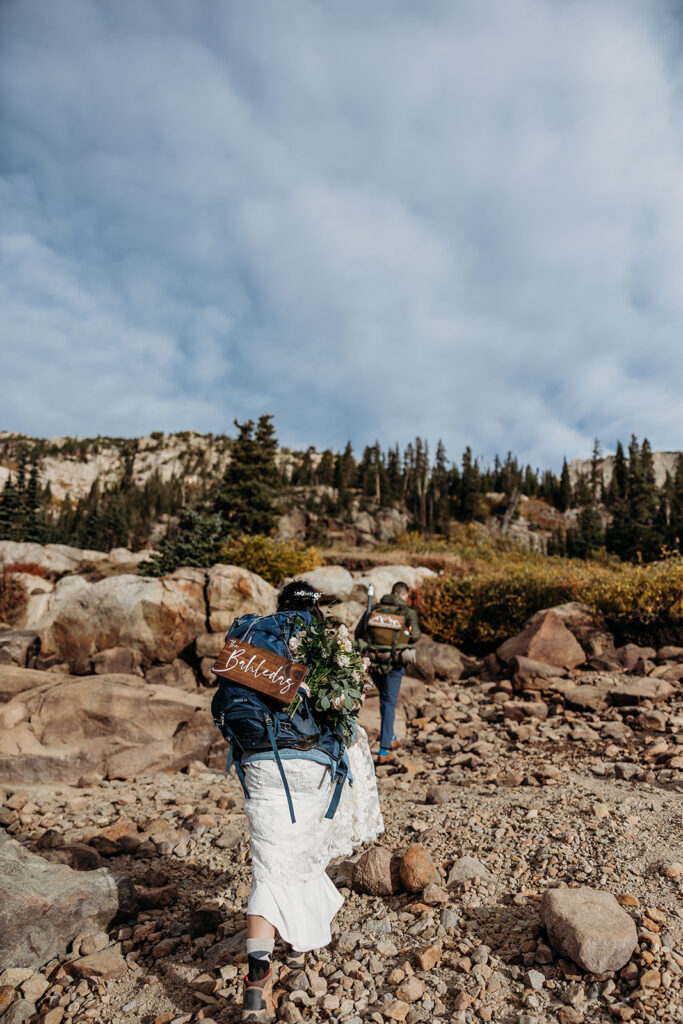 bride and groom wear back packs and hike through rocks