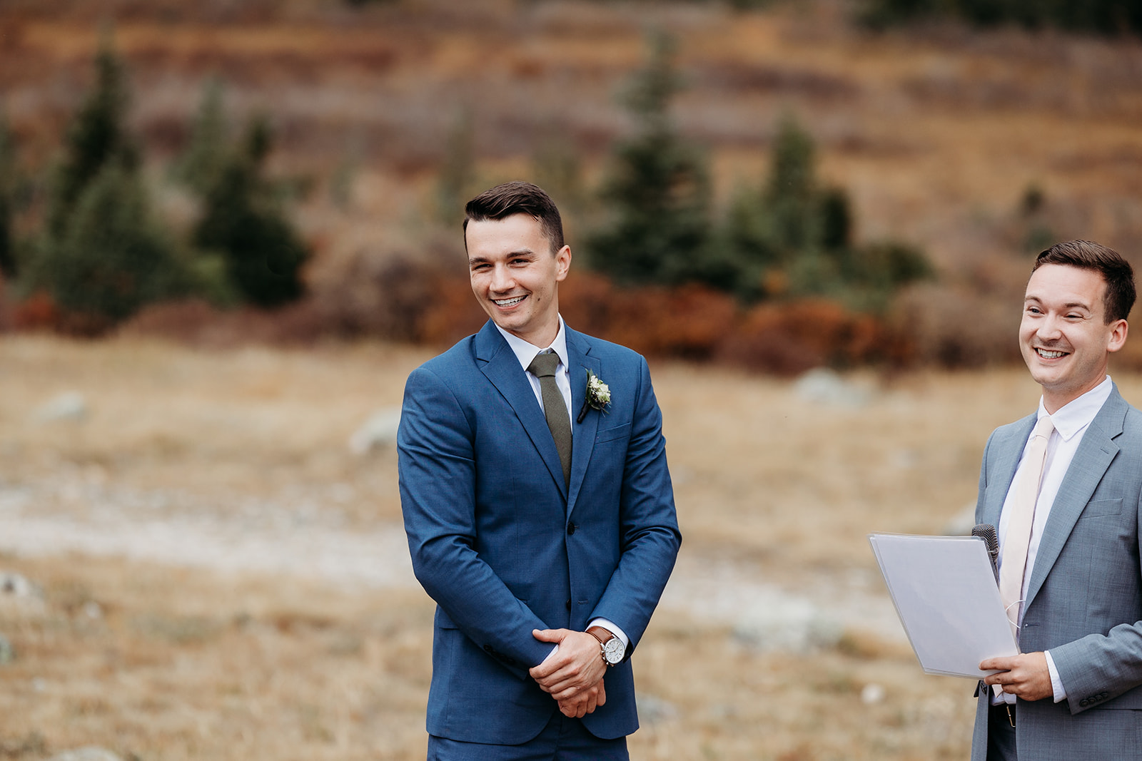 groom in blue suit stands in front of field