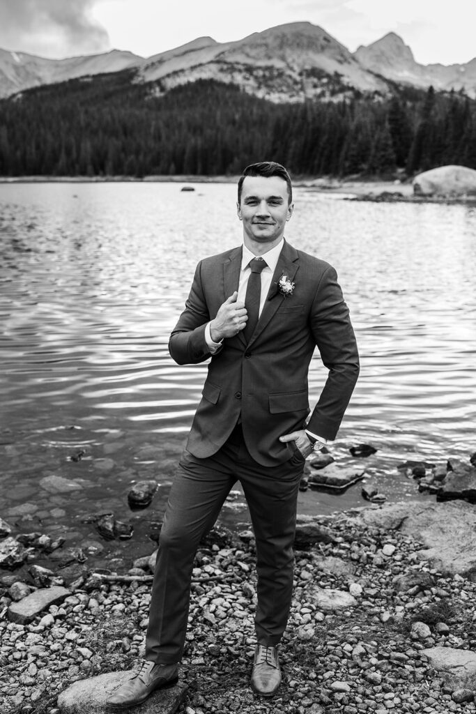 groom stands at the edge of a lake in Colorado
