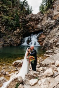 groom kisses bride on forehead in front of waterfall