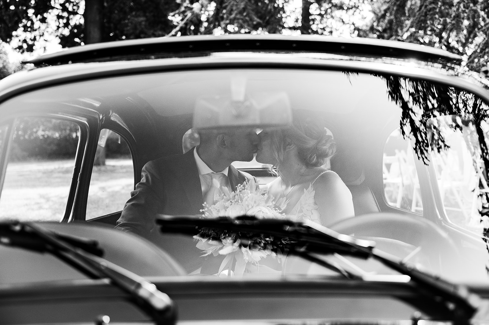 bride and groom sit in back seat of vintage car and kiss