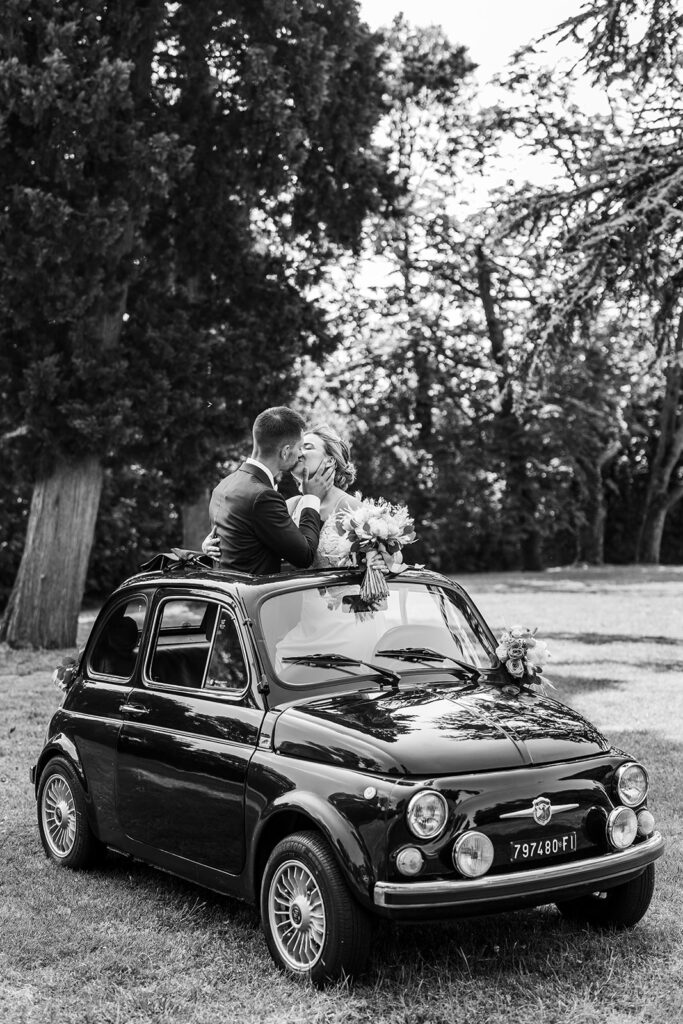bride and groom stand in sunroof of vintage car and kiss