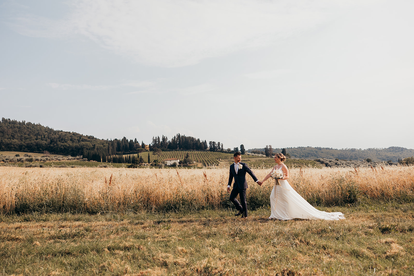 bride and groom and walk in front of field in Italian countryside