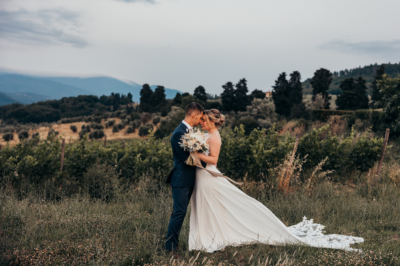 bride and groom stand embraced in front of field