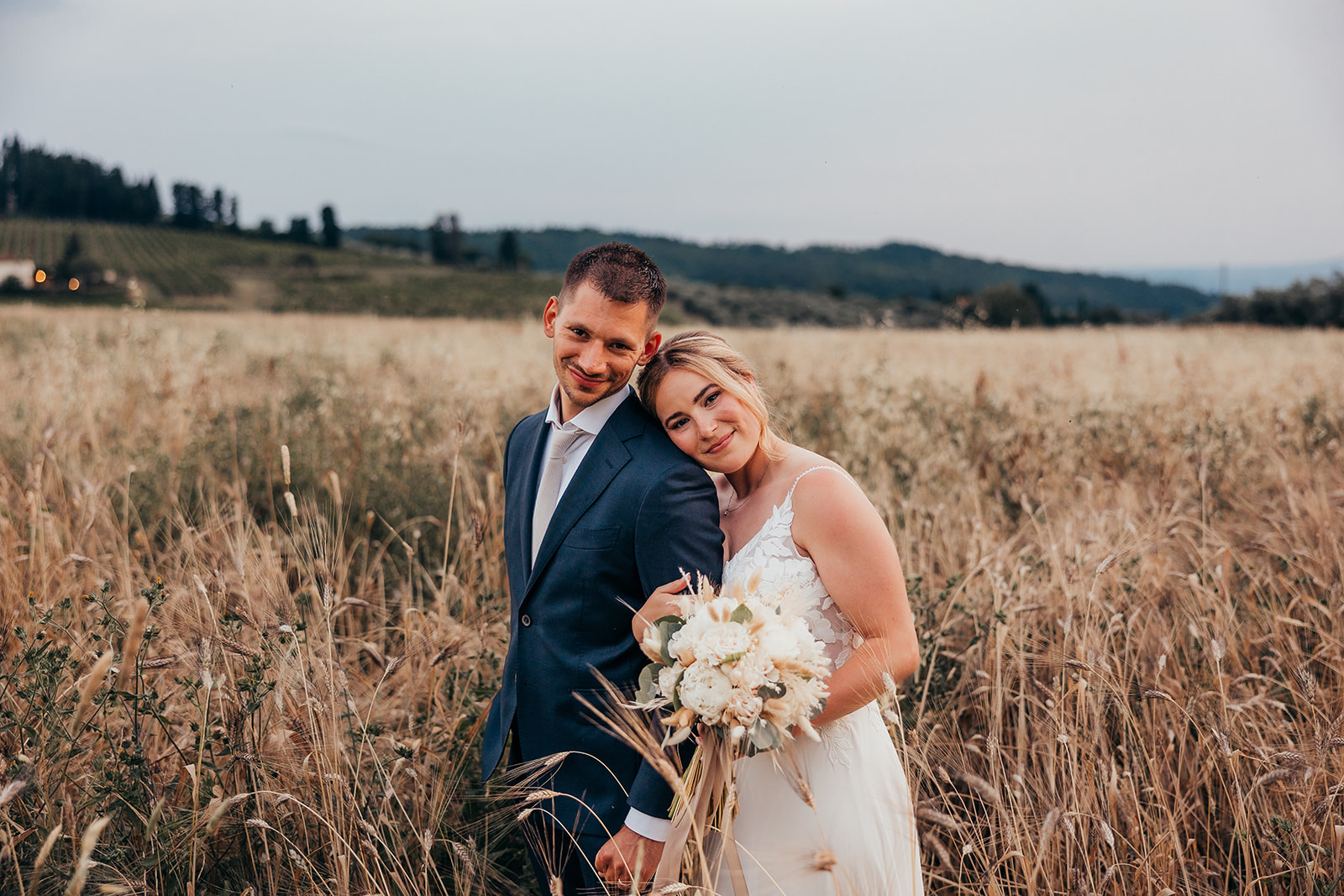 bride puts her head on groom shoulder with field behind them
