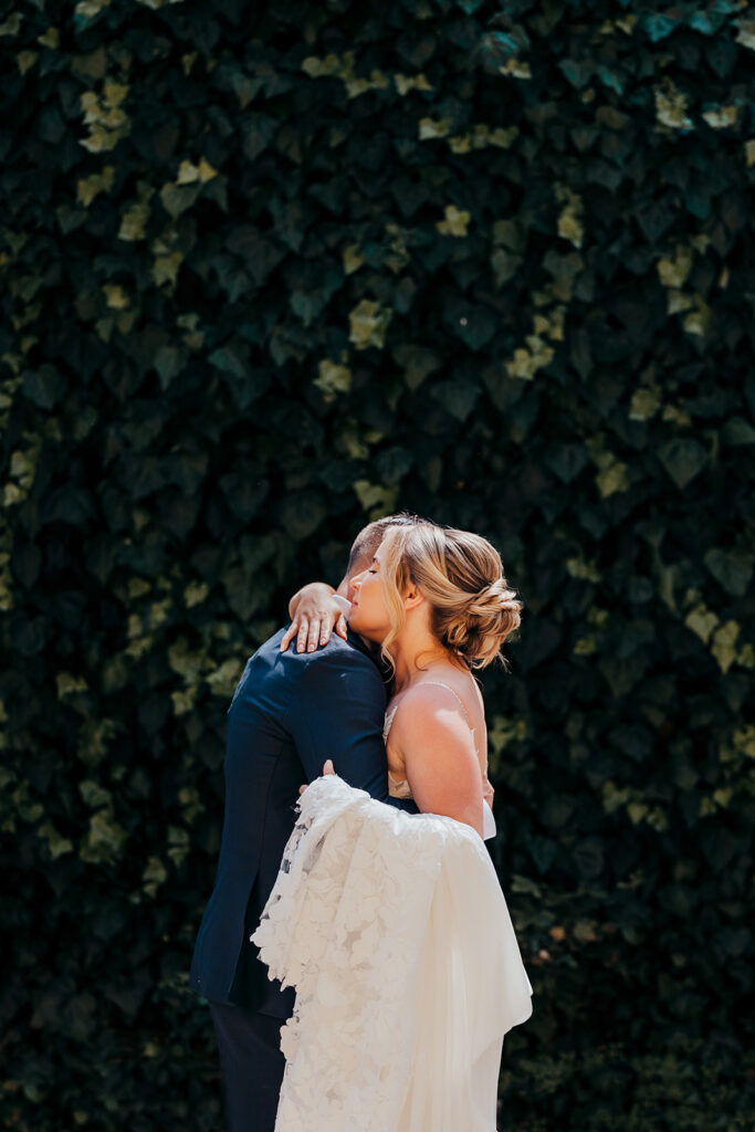 bride and groom embrace in front of wall of ivy