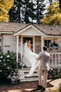 groom holds brides veil into cottage